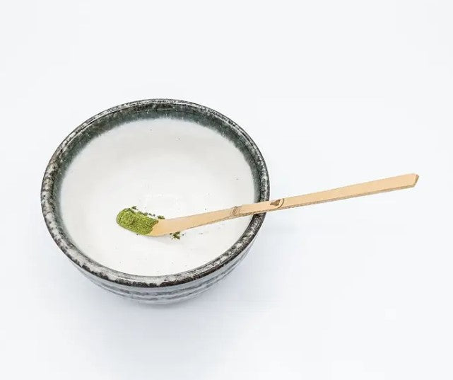 Cuchara Chashaku de bambú con polvo de matcha verde premium. Utensilio para servir la porción exacta en cuenco de cerámica artesanal