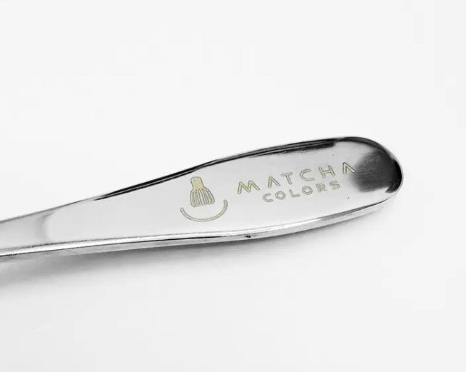 Primer plano del mango de la cuchara dosificadora. Muestra el logo y la marca Matcha Colors grabados con láser en el acero inoxidable.