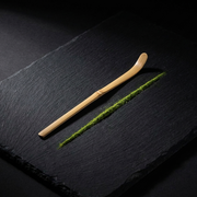 Chashaku de bambu de Matcha Colors sobre pizarra negra junto a una linea de matcha verde, composicion zen - campaña IA