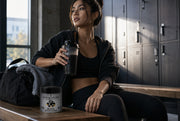 Persona con ropa deportiva sosteniendo un batido negro en el banco de un vestuario, con la lata de Black Matcha Blend al lado - campaña IA