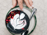 Latte negro de carbón activado con arte de corazón y pétalos de rosa, vista superior
