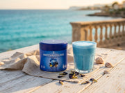 Océano en taza: Blue Matcha Blend en terraza junto al mar Mediterráneo, el latte azul a juego con el agua - campaña IA