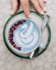 Latte de Blue Matcha Blend con arte de cisne, manos y cuchara