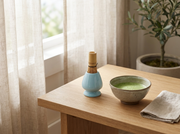 Soporte de ceramica azul de Matcha Colors con batidor chasen junto a un cuenco de matcha a la luz de la manana - campaña IA