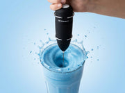 Espumador de leche electrico de Matcha Colors batiendo un vortice en un latte azul con salpicadura congelada - campaña IA
