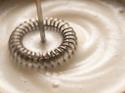 Macro del cabezal espiral del espumador electrico de Matcha Colors girando en espuma de leche cremosa - campaña IA