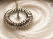 Macro del cabezal espiral del espumador electrico de Matcha Colors girando en espuma de leche cremosa - campaña IA