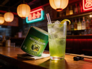 Highball helado de matcha verde junto a la lata de Green Matcha Blend en la barra de un izakaya con neones de noche - campaña IA