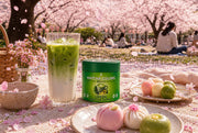 Picnic hanami bajo cerezos en flor con matcha latte helado, dulces wagashi y la lata de Green Matcha Blend - campaña IA