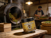 Lata de Hojicha Matcha Premium sobre un banco de madera en un tostadero artesanal de té japonés, con tambor de tostado y hojas - campaña IA