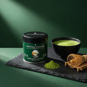 Lata de Japanese Matcha Premium sobre pizarra con cuenco de matcha batido, chasen y montón de polvo verde - campaña IA