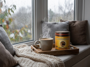 Lata de Masala Chai Caffeine Free de Matcha Colors con una taza humeante en un asiento de ventana un día de lluvia - campaña IA
