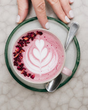Latte rosa con arte de leche, pétalos y mano sosteniendo la taza