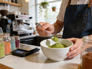 Barista dosificando matcha verde en un cuenco con la cuchara medidora de acero de Matcha Colors en una cafeteria de especialidad - campaña IA
