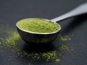 Macro de la cuchara de acero pulido espejo de Matcha Colors llena de matcha verde sobre superficie oscura - campaña IA