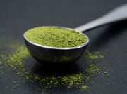 Macro de la cuchara de acero pulido espejo de Matcha Colors llena de matcha verde sobre superficie oscura - campaña IA