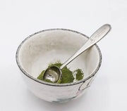 Cuchara medidora de metal con matcha verde en un cuenco de ceramica