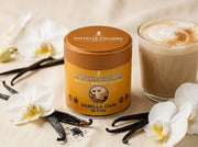 Lata de Vanilla Chai Blend de Matcha Colors rodeada de vainas de vainilla, orquídeas blancas y un chai latte cremoso - campaña IA