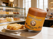 Lata de Vanilla Chai Blend de Matcha Colors sobre el mostrador de mármol de una pastelería francesa junto a éclairs de vainilla - campaña IA