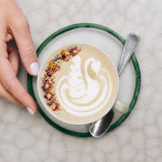 Latte blanco con arte de cisne, pétalos y manos sosteniendo la taza