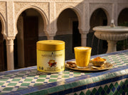 Lata de Yellow Matcha Blend con un latte dorado de cúrcuma sobre azulejos zellige en un patio estilo riad al atardecer - campaña IA
