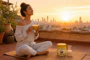 Mujer con un latte dorado al amanecer en una azotea, con la lata de Yellow Matcha Blend junto a la esterilla de yoga - campaña IA