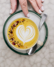 Latte amarillo con arte de corazón y mano sosteniendo la taza